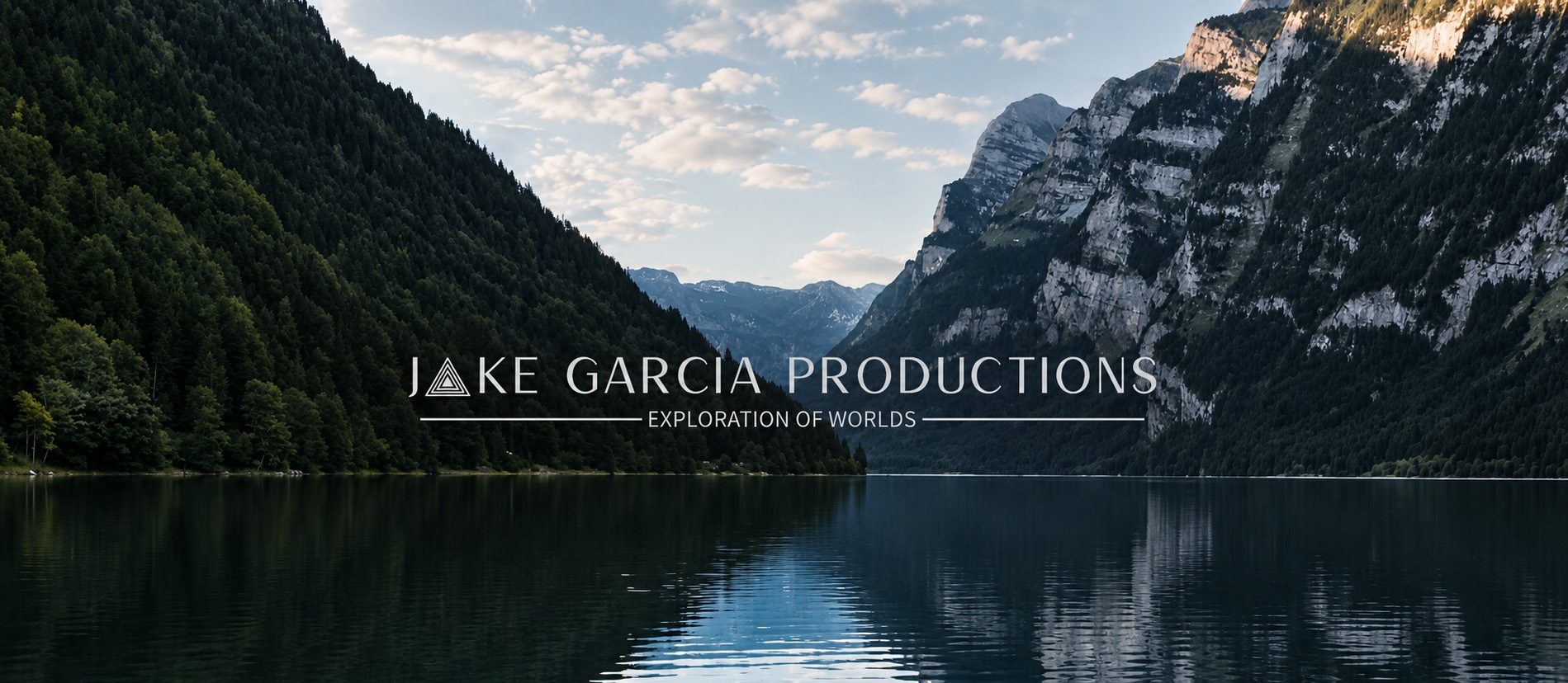Jake Garcia Productions. Exploration of Worlds. An alpine lake beneath forested mountains.