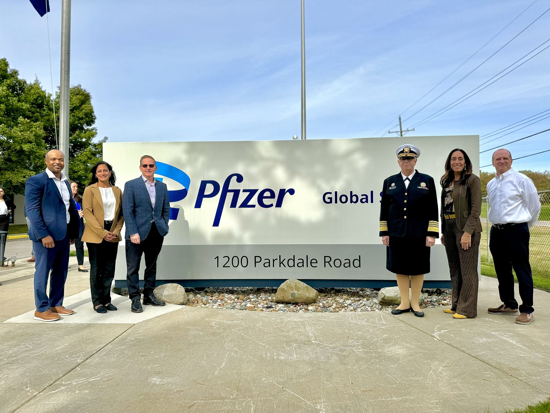 Federal health officials and Pfizer leadership standing together at the Pfizer Global Supply sign in Rochester, Michigan.